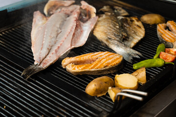Cooking seafood mix of salmon, sea bass and vegetables. Grilling fish with chili potatoes and tomato.