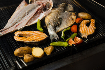Cooking seafood mix of salmon, sea bass and vegetables. Grilling fish with chili potatoes and...