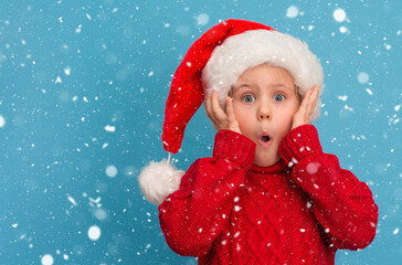 Funny surprised child in Santa hat and red sweater on blue snowy background.