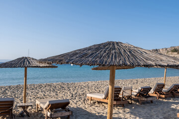 Fototapeta na wymiar Summer holiday at seaside. Straw umbrellas loungers in row on sandy empty beach sunny day.