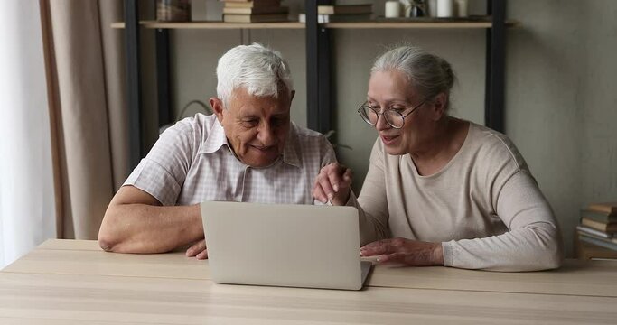 Active older married couple pensioners enjoy using laptop computer at home look at screen surf social networks read news online with interest. Bonding retired husband wife relax browse internet on pc