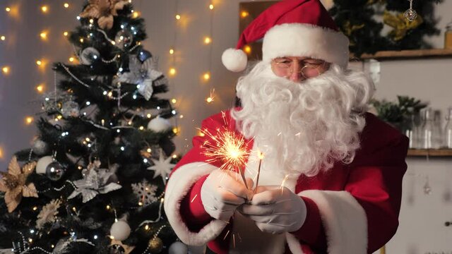 Merry Santa Claus is dancing with sparklers to celebrate Christmas. Merry, magical, children's, family holiday, Christmas. Santa Claus is having fun in a room with a Christmas tree. New Year Christmas