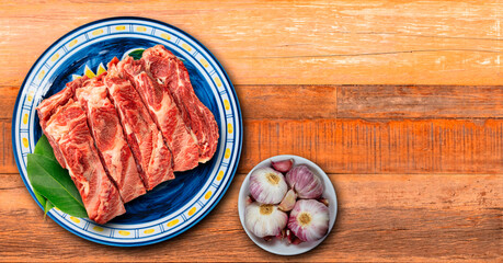 Rustic wooden table with sliced raw meat over plate and bowl with garlic.