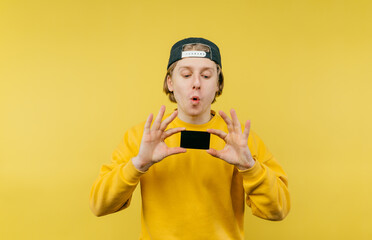 Funny guy with a surprised face holds a bank card and looks at it against the yellow wall.