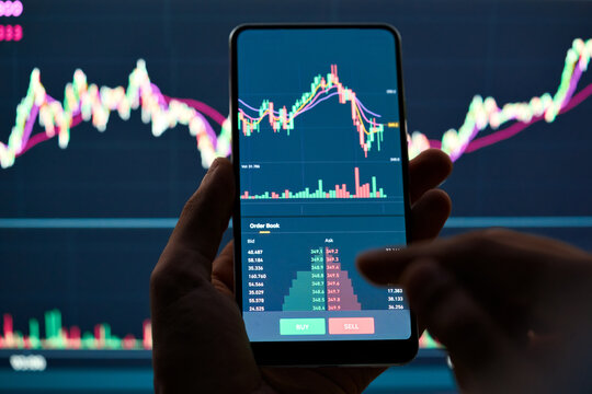 Crypto trader investor broker holding finger using cell phone app executing financial stock trade market trading order to buy or sell cryptocurrency shares thinking of investment risks profit concept.