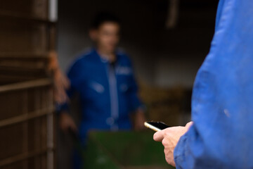 young farmer using the mobile on the farm sending a message to his clients while his coworker working is out of focus in the background. concept of technology in the farm agriculture and livestock