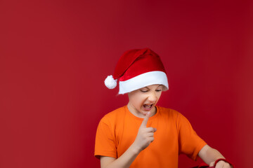 a boy in a Santa Claus Christmas hat holds a gift bag in front of him and shakes his finger