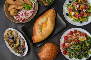 top view of khachapuri dish with cheese and egg in Adjarian with Caesar and Greek salads with potatoes and herring on the table