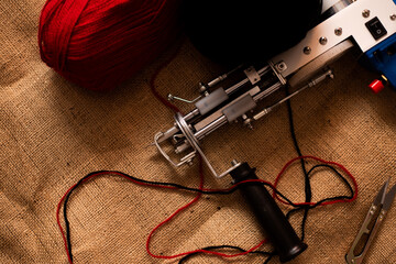 A tufting gun with red and black yarns on a sackcloth.