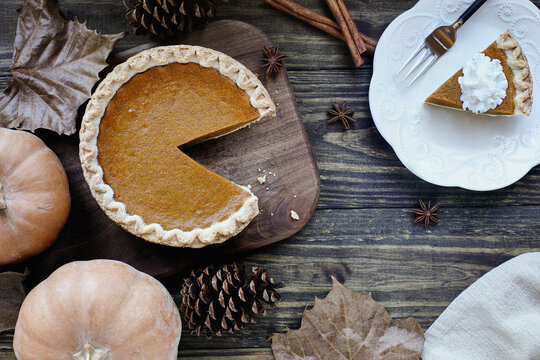 Flatlay of fresh baked pumpkin pie with slice on a plate over wood table background. Thanksgiving Day table. Top view.