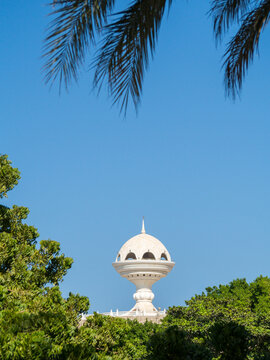 View to the Riyam Park monument dome through the palm leaves. Muscat, Oman.