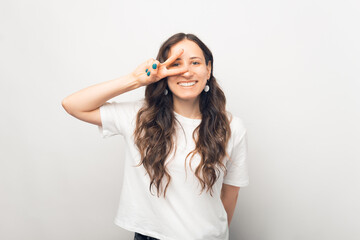 Fototapeta premium Joyful young woman in white t-shirt showing peace gesture.