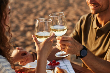 Close up of young couple drinking wine outdoors on beach while enjoying romantic date at sunset,...