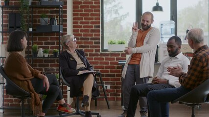 Happy man sharing progress and overcoming addiction with group of patients at aa meeting, celebrating together. People clapping hands and feeling glad about achievement at therapy session.