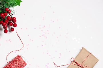 Minimalism style Christmas composition with gift box in craft paper, and holly berries on white...