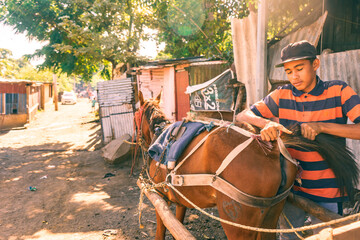 Hispanic poor boy preparing his horse used for product transportation.