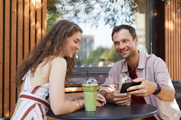 Portrait of happy couple looking at smartphone screen at outdoor cafe while enjoying date in Summer, copy space