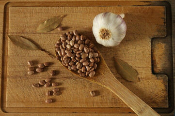Carioca beans in a wooden spoon top view. Beans with garlic bulb and dried laurel on the wooden board.