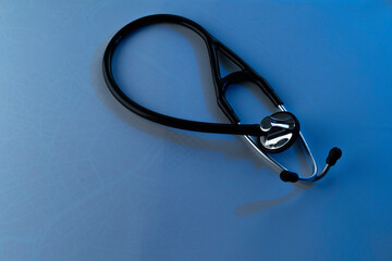 Black/silver stethoscope in diagonal position, general shot, overhead blue background