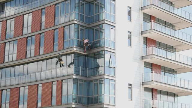 window facade glass cleaners of outside skyscraper. professional climbers in safety equipment washers on industrial high office building or residential house hotel. dangerous job occupation concept