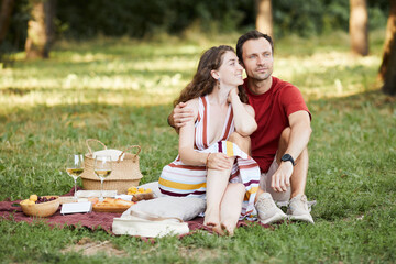 Full length portrait of happy young couple enjoying romantic picnic outdoors on green grass, copy space