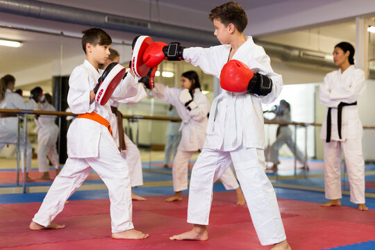 Two boys in boxing gloves launching blows during self defense workout in sport gym