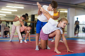Fototapeta na wymiar Sportive preteen kids practicing in pair self-protection in class with female teacher