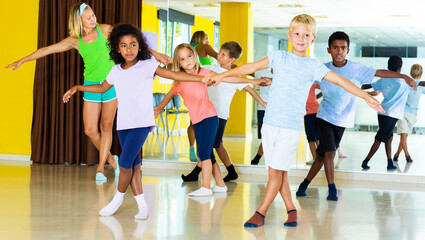 Tweenagers in pairs learning to dance active boogie-woogie with female teacher in modern studio