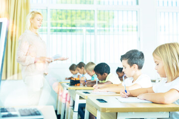 Fototapeta premium Multiracial group of kids working at class, writing and listening explanations of teacher in classroom