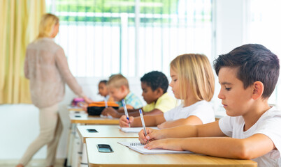 Fototapeta premium Side view of schoolkids group working on lecture in classroom, making notes