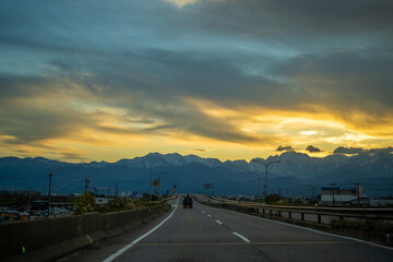 Fototapeta premium 富山県富山市の道路から朝焼けの剱岳や立山を見る風景 View of Tsurugidake and Tateyama in the morning sun from the road in Toyama City, Toyama Prefecture, Japan.