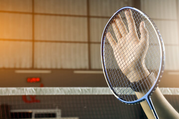 Badminton player raises hand and racket to show respect to another player opposite court and thank you to audiences after games or competition. Soft and selective focus.