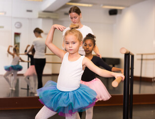 Fototapeta na wymiar Female ballet trainer teaching two little girls near ballet barre in dancing hall