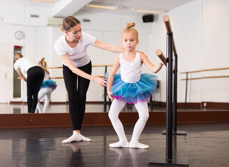 Fototapeta na wymiar Female classical dance trainer teaching little ballerina in ballet class.