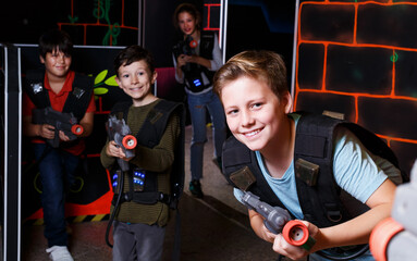 Fototapeta na wymiar excited sportive young boy aiming laser gun at other players during lasertag game in dark room