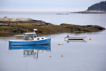 Tranquil scene in coastal Maine.  Blue lobster boat and small dinghy anchored alongside rocky...