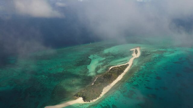 Very high up drone shot of a tiny island Cresta de Gallo and its coral reef with thin clouds drifting in front of camera.