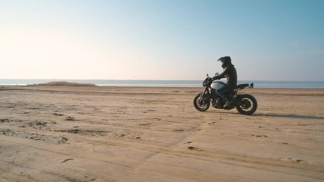 Motorcyclist driving his customized fast motorbike on the dirt road in desert around sea or lake. Slow motion