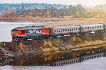 Passenger train moves along the lake at autumn morning. Karelia.
