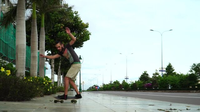 Millennial guy with man bun and beard skateboarding on empty sidewalk. Slow mo