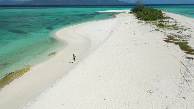Young and fit man runs down the perfectly white sand beach on a small tropical deserted island Cresta de Gallo in The Philippines
