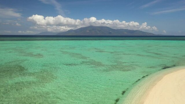 Young man standing alone on the beach, looking over the colorful and crystal clear water with fluffy clouds and mountains in the distance. Cresta de Gallo