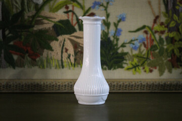 Small white milk glass vase on table in front of embroidered artwork