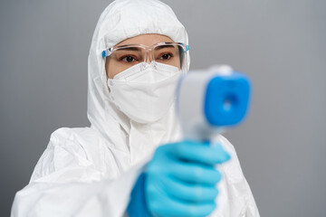 doctor in protective PPE suit scanning with infrared thermometer