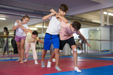 Obraz premium Kids exercising self-protection moves during group training in gym.