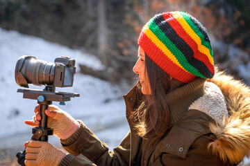 Young woman videographer in rasta hat photographing outdoors with steadicam