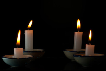 Picture of a white candle on a cup with the light of a yellow candle flame on a black background. Ideas for Halloween, Christmas, Home, Romance, Love, Copy space for you