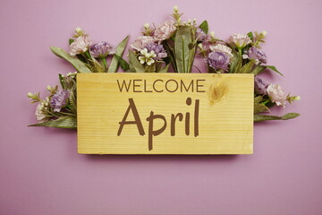 Welcome April text on wooden board with flowers frame on purple background