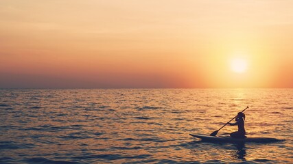 Silhouette of young woman playing paddle board in sea with the sunset sky background.Water sports concept And travel in the summer.