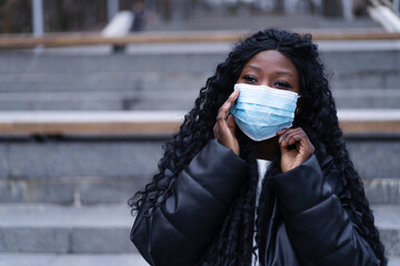 Young Afro girl with face medical mask in a outdoors. African girl using facemask for preventing and stop corona virus spread. Health care people concept